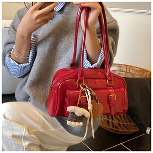 Close-up of red patent leather underarm bag featuring decorative charms and buckles