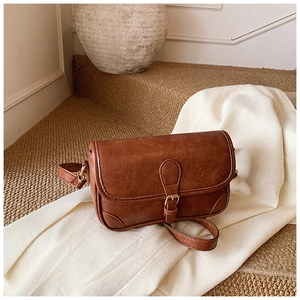 Close-up of caramel brown leather crossbody bag with vintage buckle on soft fabric