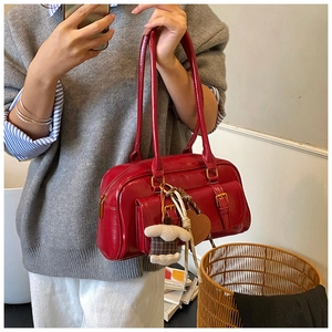 Detail of red glossy shoulder bag featuring dual front pockets and heart charm
