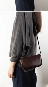 Detailed side view of dark brown leather crossbody bag worn by a model in soft light