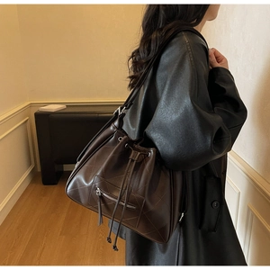 Detail of dark brown quilted drawstring bucket bag shown on a model for scale and style