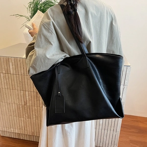 Minimalist black leather tote bag with long shoulder straps shown on a model