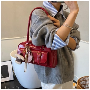 Detail of red patent leather shoulder bag with a heart charm and double buckle front pockets