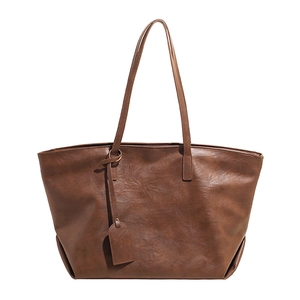 Brown textured leather tote bag with long shoulder straps and decorative charm on white background