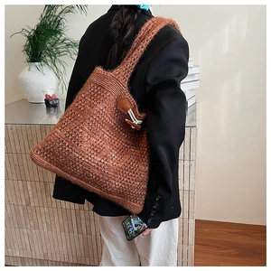 Close-up of caramel knit tote bag showing thick stitch texture and leather toggle detail
