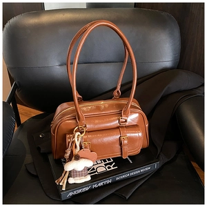 Detailed view of a brown leather shoulder bag with decorative charms on a vintage book