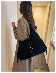 Dettaglio di una borsa tote in pelle scamosciata nera con borchie e frange su modella