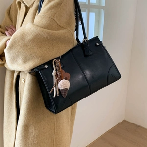 Grand sac cabas minimaliste en cuir noir porté par un mannequin en manteau de laine
