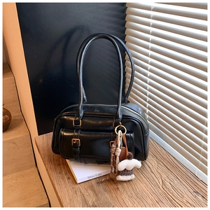 Detailed view of a black retro underarm bag with gold buckles and plush charm on wood