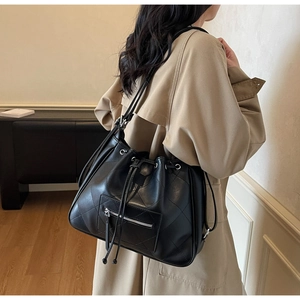 Detail of black quilted drawstring tote bag with zipper front pocket on tan coat