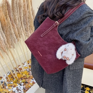 Burgundy suede tote bag with white stitching and plush rabbit charm in autumn setting