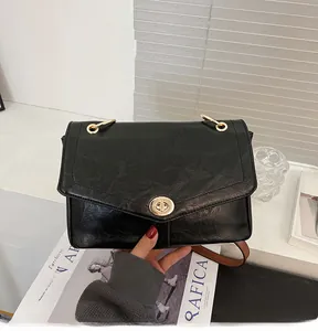 Détail d'un sac à bandoulière noir brillant avec fermoir rotatif en métal doré rond