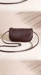 Detail of dark brown leather crossbody bag with visible white stitching and crescent shape