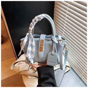 Detail of light blue bucket bag with decorative silk scarf and golden twist lock closure