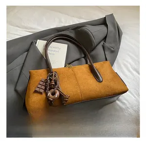 Detail view of camel suede tote bag featuring chocolate and donut charms on white bedding