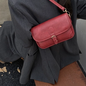 Retro burgundy faux leather crossbody bag with metal buckle on grey blazer