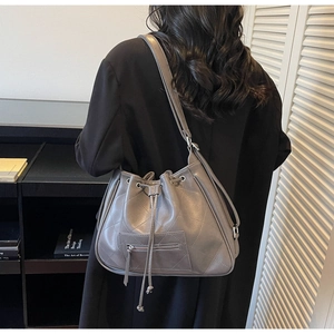 Close-up of gray quilted drawstring tote bag worn over the shoulder on a black blazer