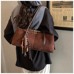 Close-up of brown suede shoulder bag with chocolate charm and woven rope detail