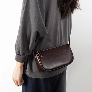 Deep brown leather crossbody bag with minimalist semi-circular design and adjustable strap