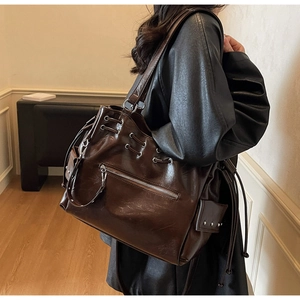 Detail of dark brown tote bag with silver studs and zippers on a model's shoulder
