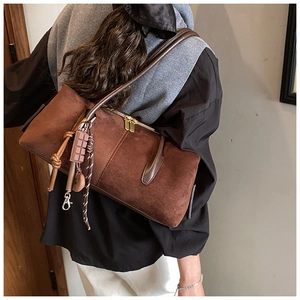 Detail of a brown suede shoulder bag with dual metal zippers and unique decorative charms