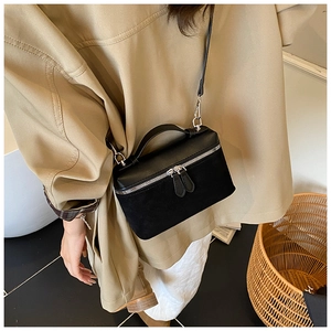 Detail of black suede vanity case bag with silver dual zippers and top handle worn by model