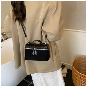 Detail view of a black leather and suede crossbody bag with dual zippers and top handle