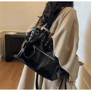 Detail of glossy black tote bag featuring silver metal grommets and functional zippers