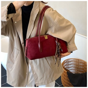 Close-up of deep red suede shoulder bag with gold zippers held by a model in a trench coat