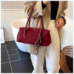 Detail of dark burgundy suede shoulder bag showing matte texture and woven charm
