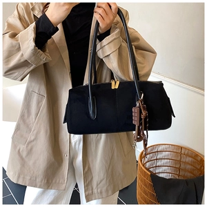 Detail of minimalist black faux suede shoulder bag with gold zippers and chocolate charm