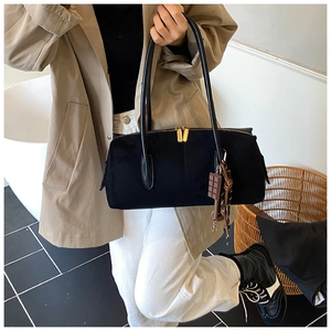 Detail of black textured shoulder bag with golden zipper and chocolate charm accessory