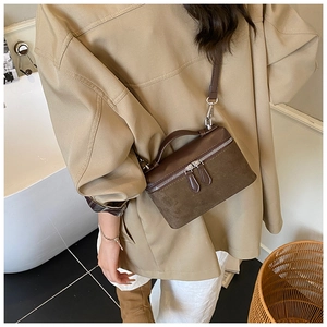 Detail of a brown suede small square handbag with dual zippers and a top handle