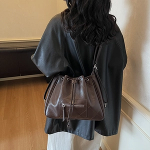 Quilted drawstring tote bag in dark brown faux leather shown on shoulder in interior setting