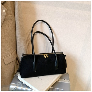 Detailed view of black suede shoulder bag with dual gold zippers on a silver suitcase