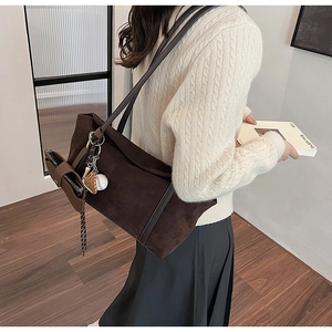 Detail of dark brown suede tote bag with leather strap and baseball charm on a model
