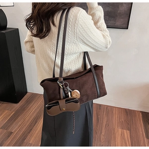Detail of dark brown matte suede tote bag with leather straps and bear charm