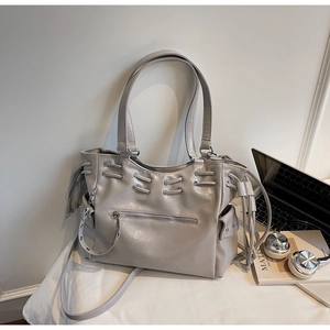 Close-up of stylish grey tote bag with metal eyelets and zippers in a workspace setting