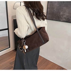 Detail of dark brown suede tote bag with stylish baseball charm on shoulder