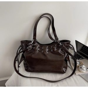Detail of dark brown tote bag with metal eyelets and adjustable strap in office setting