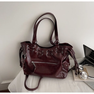 Detail of burgundy glossy leather tote bag showing silver zippers and metal grommet decor