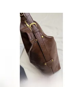 Détail du sac en cuir marron foncé avec boucles dorées et coutures soignées