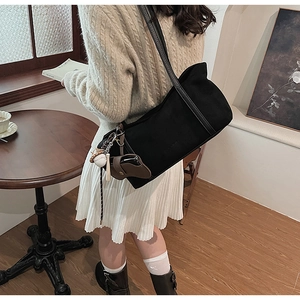 Detail of black canvas underarm bag with leather strap and baseball charm on a model