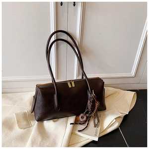 Detail of dark brown leather tote with dual straps and gold zippers on white blazer