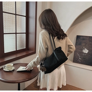 Detailed view of black tote bag with cute puppy pendant worn by model in a cafe