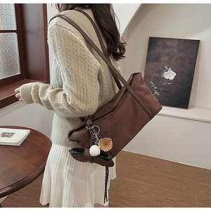 Close-up of brown suede shoulder bag with baseball charms on a soft beige sweater