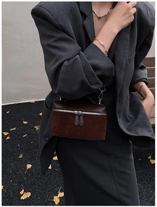 Detail of dark brown square crossbody bag with silver zippers on a grey blazer model