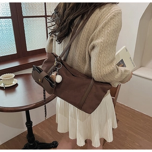 Detail of a brown suede tote bag featuring a baseball charm and small matching pouch