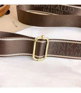 Gros plan sur la bandoulière tressée marron avec boucle dorée et lettrage de la marque