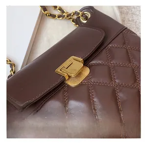 Détail d'un sac à main matelassé en cuir marron foncé avec fermoir doré et chaîne